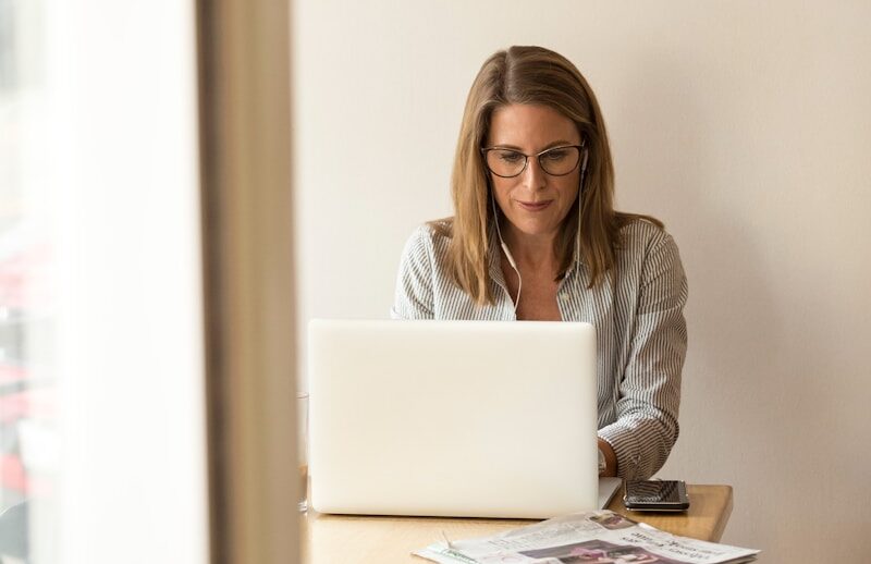 woman wearing grey striped dress shirt sitting down near brown wooden table in front of white laptop computer